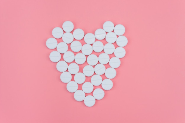 Heart made of white pills on a pink background. The concept of prevention and treatment of heart disease.