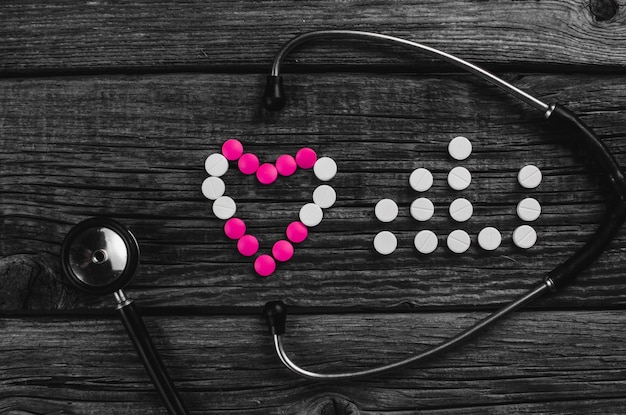 Heart and pulse of white and pink tablets and stethoscope on wooden surface