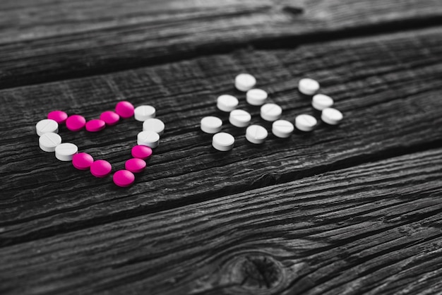 Heart and pulse of white and pink tablets and stethoscope on wooden surface