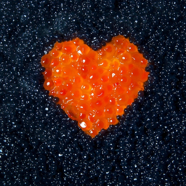 Heart of red caviar on a background of black caviar