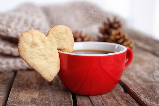 Heart shape cookie on cup of coffee on wooden table closeup