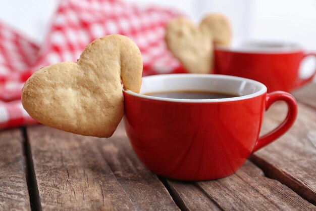 Heart shape cookie on cup of coffee on wooden table closeup