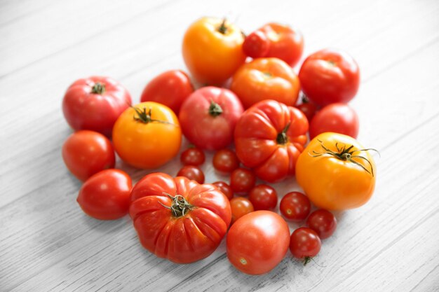 Heart shape of different tomatoes on light wooden background