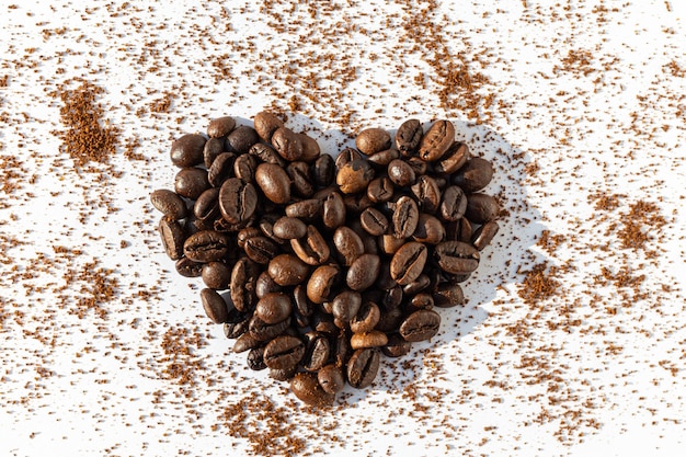 Heart shape from brown roasted coffee beans Robusta Arabica coffee on a background of ground coffee on a white background Coffee love concept