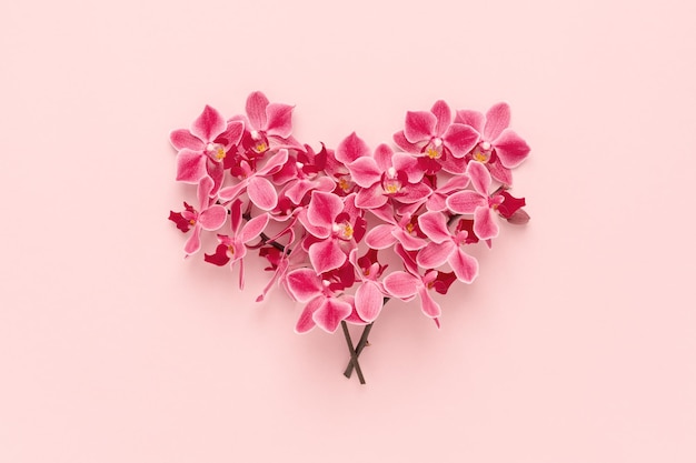 Heart shape made of Orchid flowers bouquet on pink Valentines day background. Flat lay.