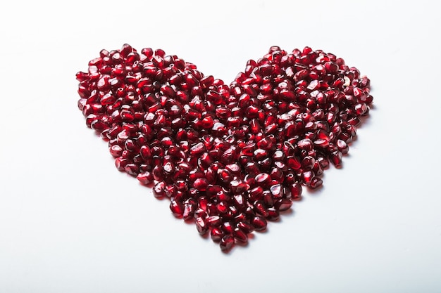 Heart shape pomegranate seeds on white.