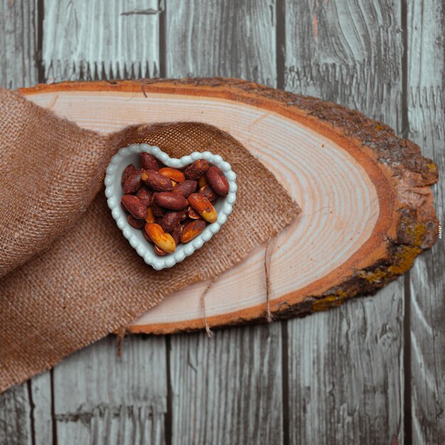 A heart shaped bowl with nuts on a wooden surface