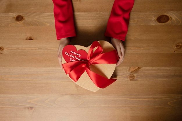 Heart-shaped box decorated with red satin ribbon in children's hands, Happy Valentine's Day card