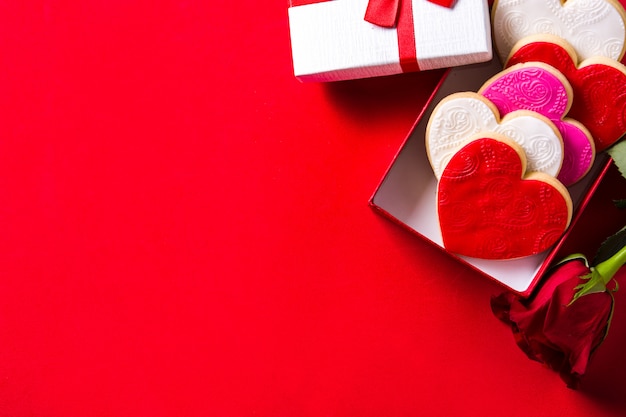 Heart-shaped cookies for Valentine's Day and roses in gift box on red, top view 