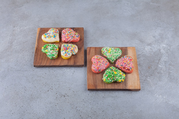 Heart shaped cookies with colorful sprinkles placed on wooden board .