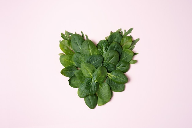 Heart shaped fresh spinach leaves on the pink