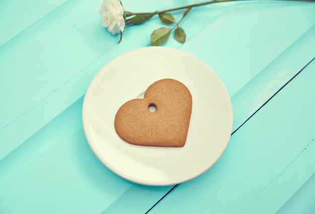 Heart shaped gingerbread cookie on white plate top view Old wooden table