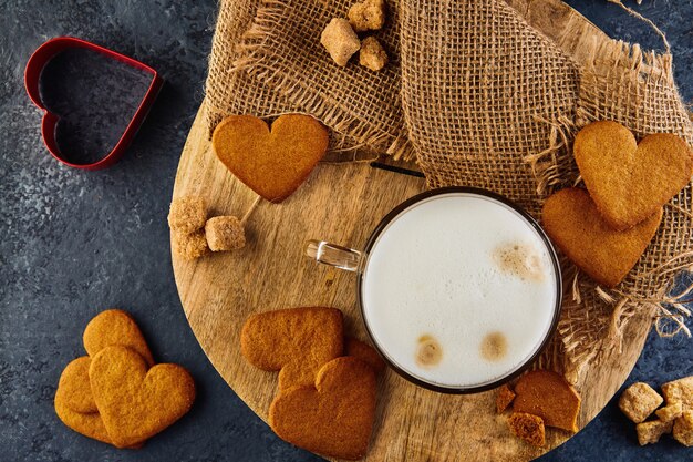 Heart shaped gingerbread cookies with a cup of cappuccino coffee on a wooden board