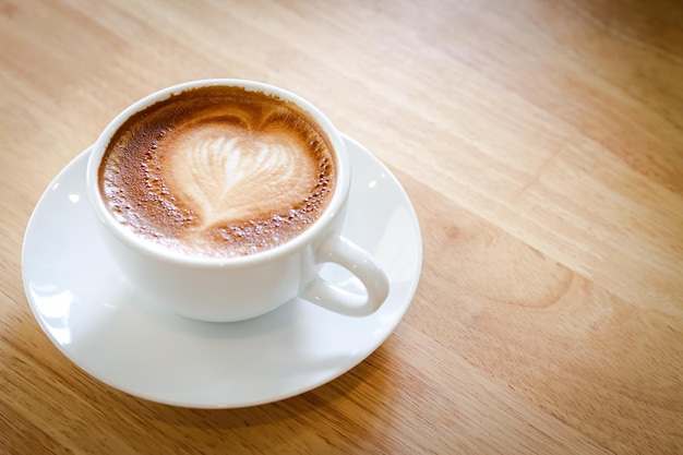 Heart shaped hot coffee latte in a white mug placed on a wooden floor Copy space