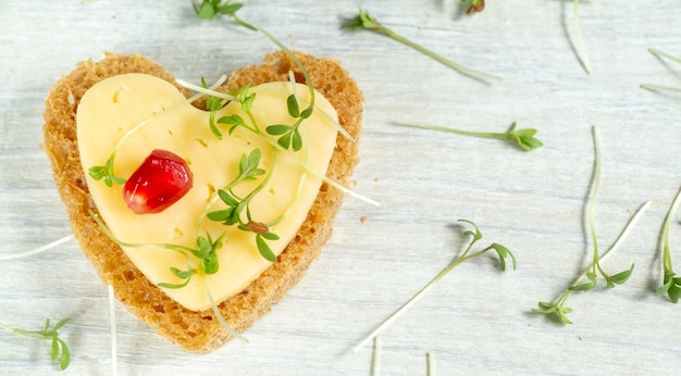 Heart shaped mini canapes with butter, cheese and watercress micro greens on a white wooden table. View from above. 