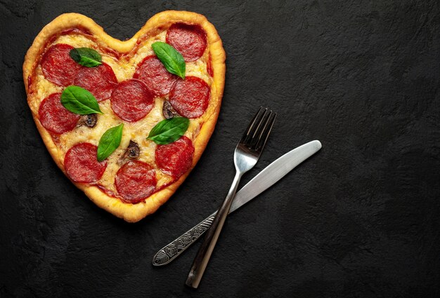 Heart shaped pizza on a black stone . Valentine's day romantic love concept