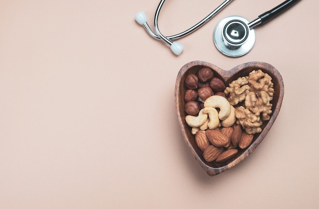 Heart shaped plate with handful mixed nuts and medical stethoscope on beige background