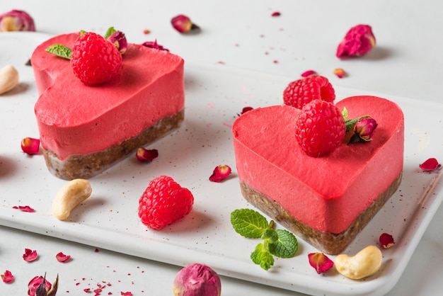 Heart shaped red raw vegan cakes with fresh raspberries, mint and dried flowers. Valentines day dessert. close up