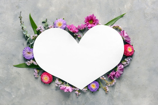 Photo heart shaped sheet of paper with beautiful flowers on grey background