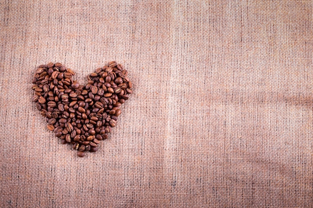 Heart with roasted coffee beans on the burlap background