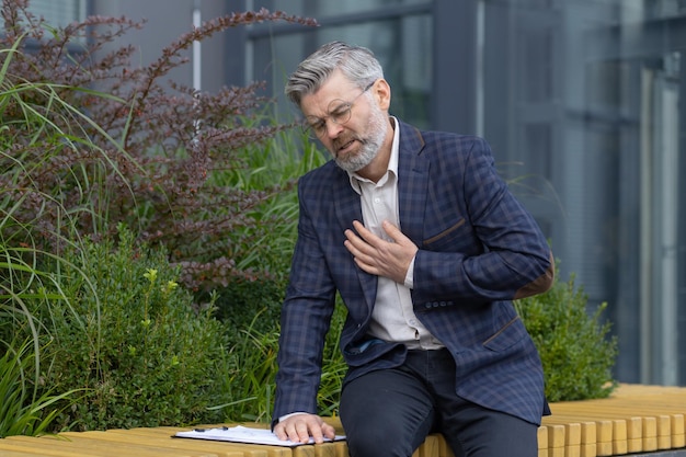 Heartache of mature man gray haired businessman holding hands on rough heart attack pain boss