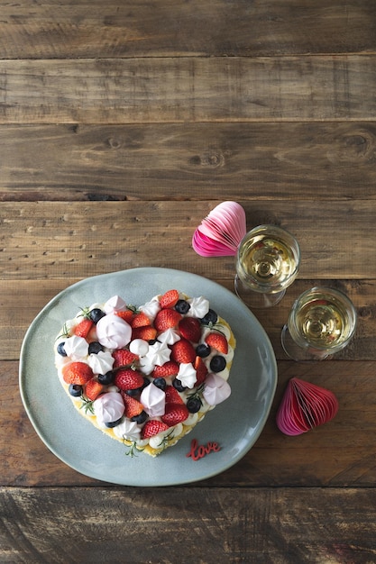 Heartshaped cake decorated with red fruits and meringue Rustic wooden background Valentine's Day Copy space Vertical photo