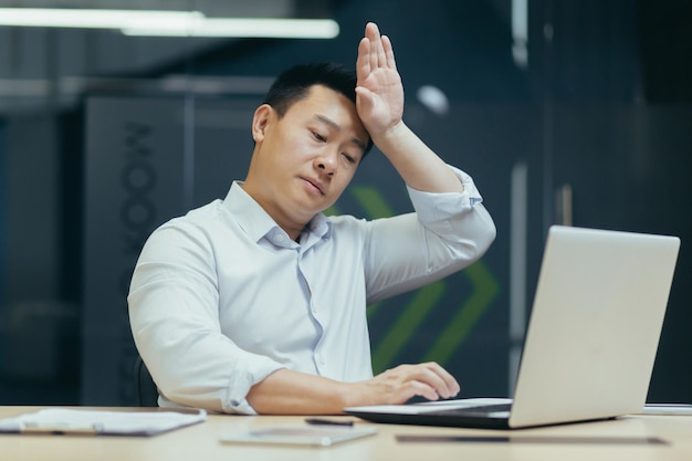 Heat and lack of air in the office an asian man works on a laptop it is hot and there is no air