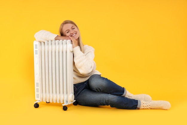 Heating season woman near heater on yellow background