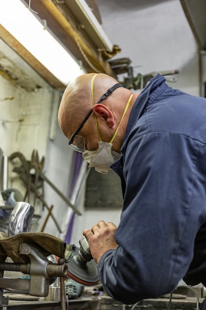 Heavy industry worker cutting steel with angle grinder at car service