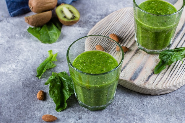 Helathy Green Smoothie with green apple, spinach, kiwi and almond nuts on gray concrete background. 