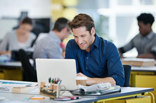 Hell tackle any project Shot of a designer sitting at his desk working on a laptop with colleagues in the background