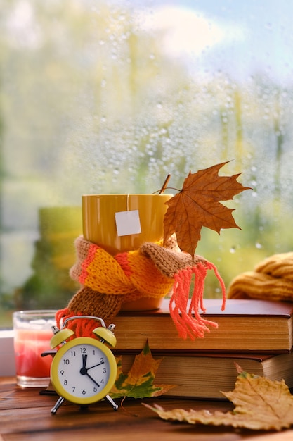 Hello Autumn. Yellow alarm clock, cup of tea on books near the window, it's raining