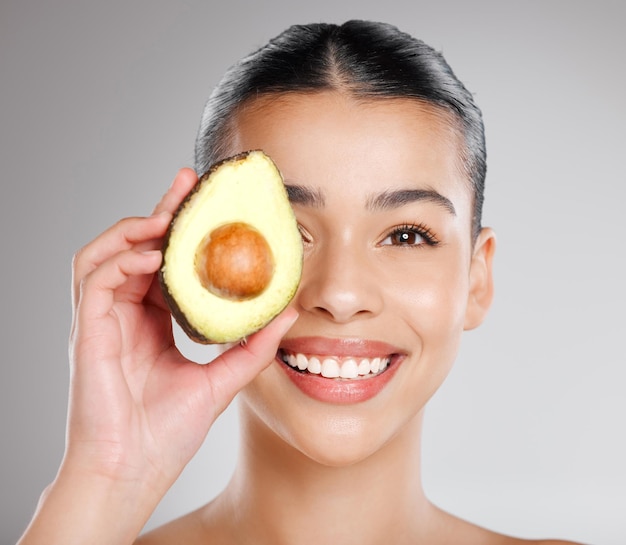 Hello skincare powerhouse avo Studio shot of an attractive young woman holding an avocado to her face against a grey background