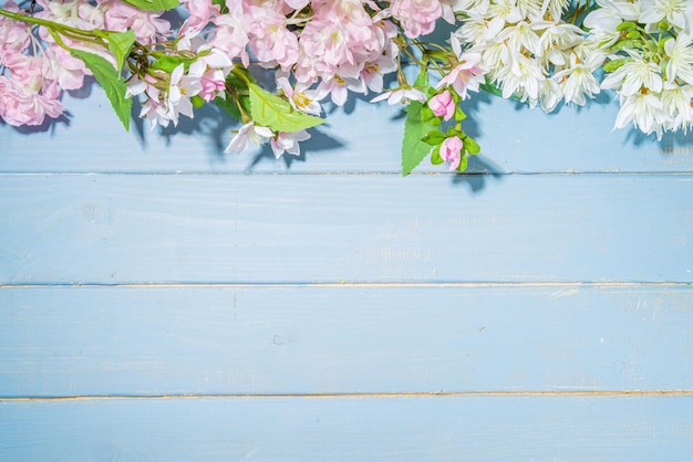 Hello spring concept Spring holidays greeting card simple flatlay background with artificial blossom spring flowers on light blue wooden garden table background frame copy space top view