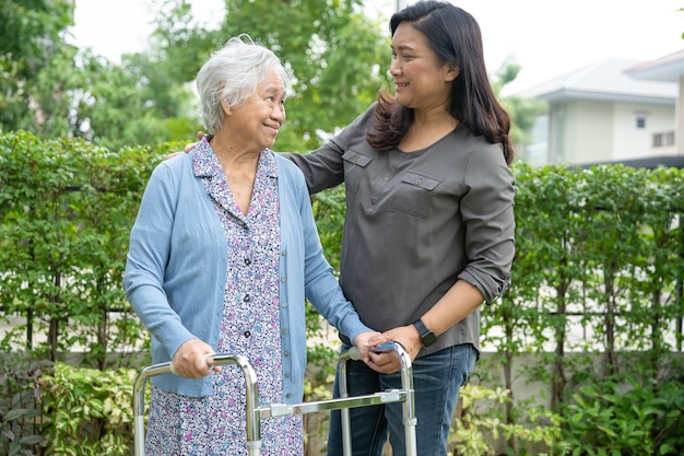 Help and care Asian senior or elderly old lady woman use walker with strong health while walking at park in happy fresh holiday.