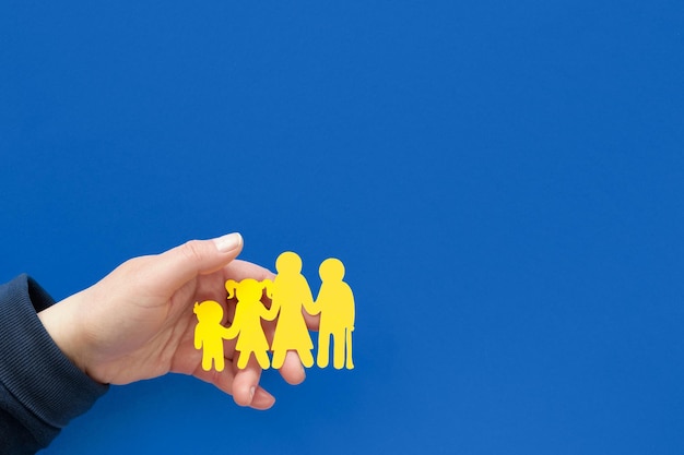 Helping hand holding Ukrainian family yellow paper silhouette Flat lay top view on blue background