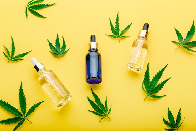 Hemp oil serum in glass dropper with cannabis leaf. Cannabis leaves with cosmetic products on yellow background.