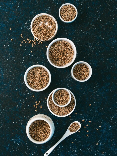 Photo hemp seeds in small white bowls and spoon on dark blue tabletop set of small bowls with raw organic unrefined hemp seed superfood and vegan concept top view or flat laycopy space for textvertical