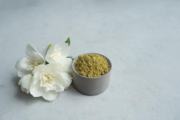 Photo henna powder for dyeing hair and eyebrows and drawing mehendi on hands on a gray cement pedestal with dried flowers or a white flower.