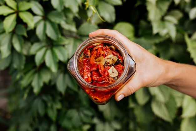 In her hand is an open jar of sun-dried tomatoes with olive oil.