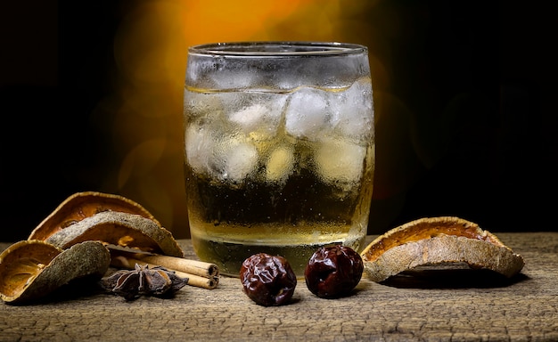 Herbal juice and fruit in a glass filled with ice and dried fruit and dried herbs placed on an old wooden table on blur bokeh background.