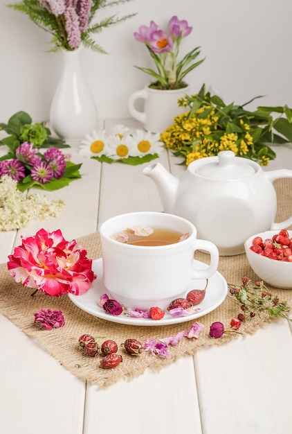 Herbal tea with rosehip chamomile and meadowsweet in a white cup on a white wooden table with flowers