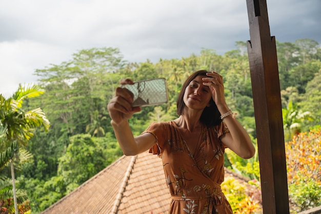 Here i am. Cheerful girl enjoying exotic nature on the island, taking photo on her gadget