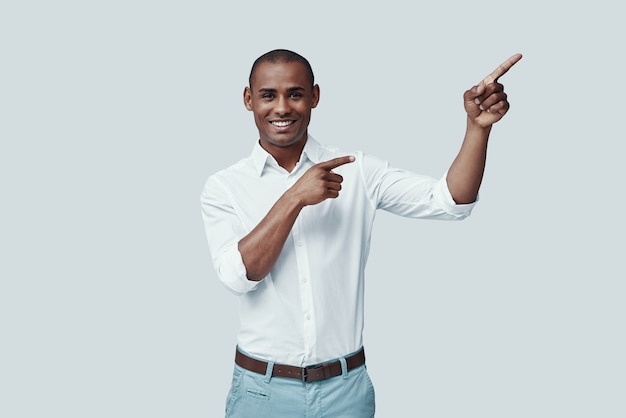 Here is something special. Handsome young African man pointing copy space and smiling while standing against grey background