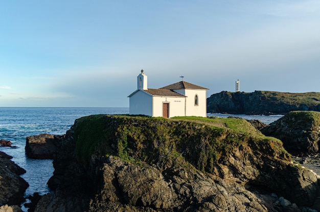 Hermitage on some cliffs on the Galician coast with the Frouxeira lighthouse in the background