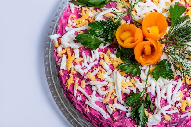 Herring salad under a fur coat on a glass dish on a white table.