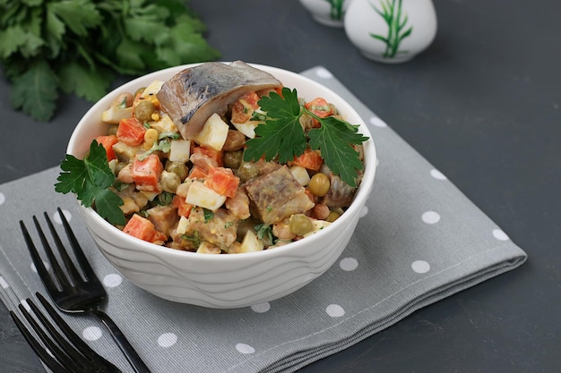 Herring salad with carrots eggs and peas in a white bowl on a dark gray background