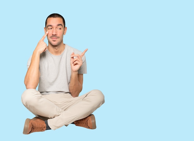 Hesitant young man making a gesture of being careful with his hand pointing at his eye