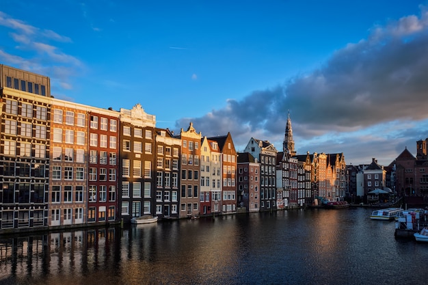 Hhouses and tourist boats on Amsterdam canal pier Damrak on suns