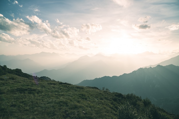 High altitude pasture, rocky mountain peaks and jagged ridge, with scenic sky, the Italian Alps. Expansive view in backlight. Toned desaturated image.